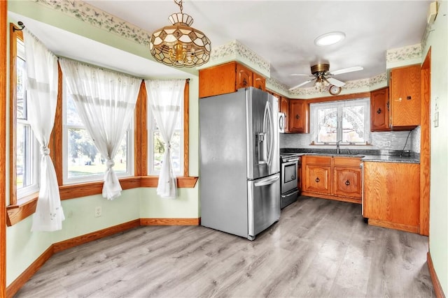 kitchen featuring light wood-type flooring, appliances with stainless steel finishes, brown cabinets, and dark countertops