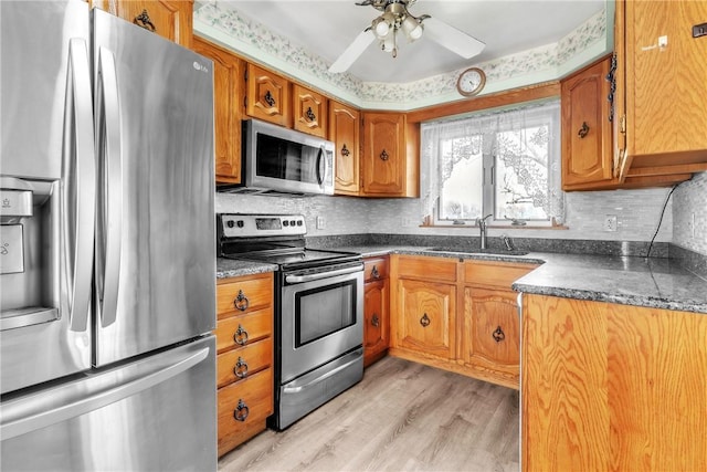 kitchen with brown cabinets, dark countertops, appliances with stainless steel finishes, and a sink