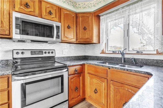 kitchen with brown cabinetry, backsplash, appliances with stainless steel finishes, dark countertops, and a sink