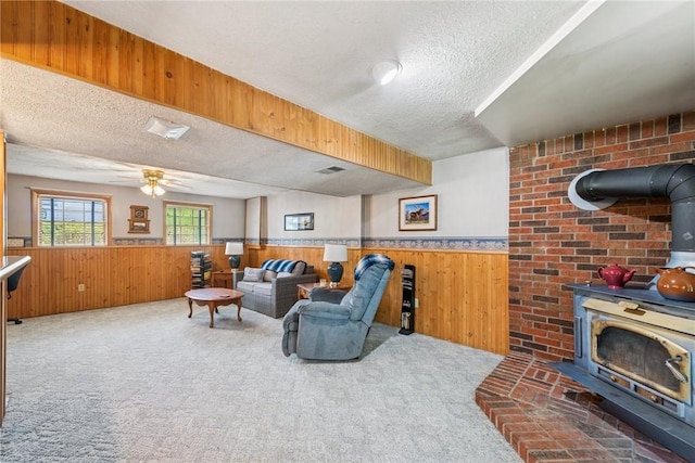 living area featuring a wood stove, a textured ceiling, a wainscoted wall, and wood walls