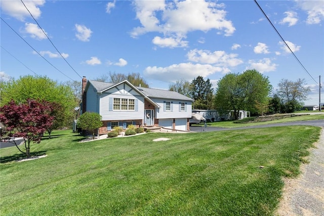 bi-level home featuring driveway, a chimney, brick siding, a front lawn, and an attached garage