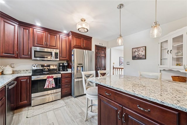 kitchen featuring light stone countertops, stainless steel appliances, light wood finished floors, and decorative light fixtures