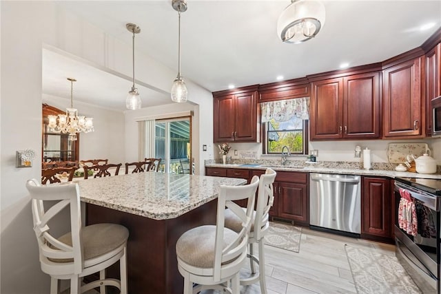 kitchen with appliances with stainless steel finishes, an inviting chandelier, a sink, light stone counters, and a kitchen breakfast bar
