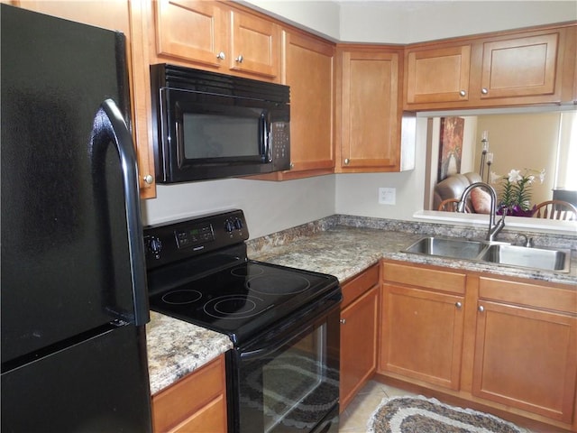 kitchen with light stone countertops, a sink, brown cabinetry, light tile patterned floors, and black appliances