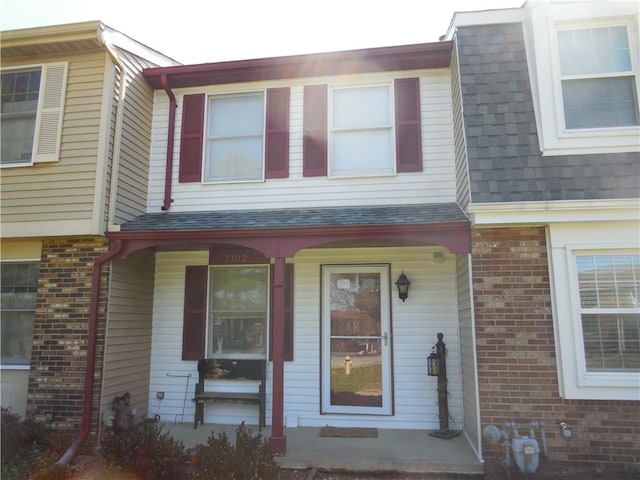 townhome / multi-family property featuring brick siding, a shingled roof, and a porch