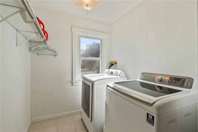 clothes washing area featuring laundry area, baseboards, light tile patterned floors, and washing machine and dryer
