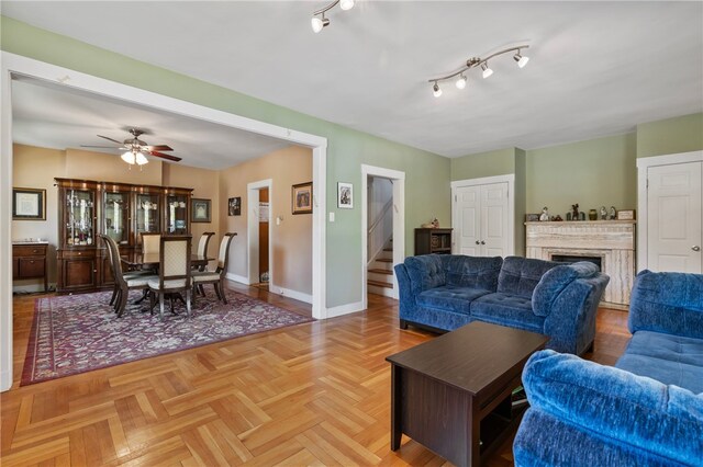 living area with baseboards, ceiling fan, a fireplace, and stairs