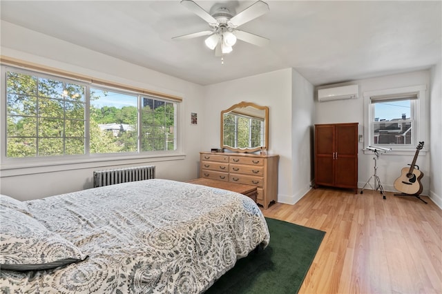 bedroom with light wood finished floors, a wall mounted AC, radiator heating unit, and multiple windows