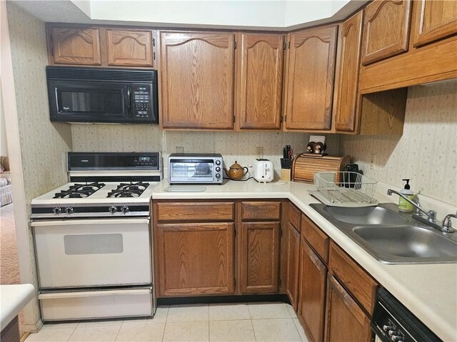 kitchen with a toaster, black microwave, wallpapered walls, white range with gas cooktop, and a sink