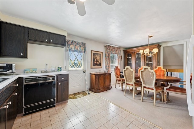 kitchen with light tile patterned flooring, black dishwasher, light countertops, ceiling fan with notable chandelier, and decorative light fixtures