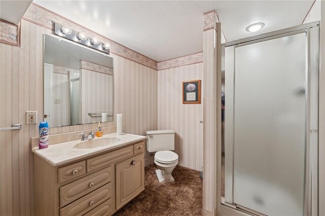 bathroom with toilet, wallpapered walls, a shower stall, and vanity