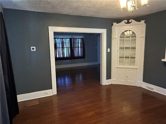 unfurnished dining area featuring dark wood-type flooring, a textured ceiling, baseboards, and a chandelier