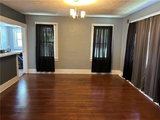 unfurnished dining area featuring visible vents, a textured ceiling, wood finished floors, and a chandelier