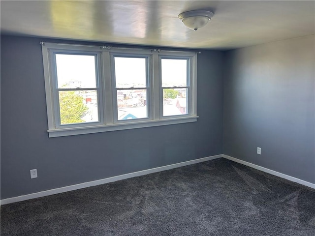 spare room featuring baseboards, a healthy amount of sunlight, and dark colored carpet