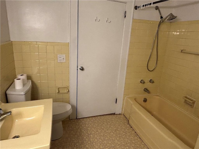 full bath featuring tile walls, bathtub / shower combination, a sink, a wainscoted wall, and toilet