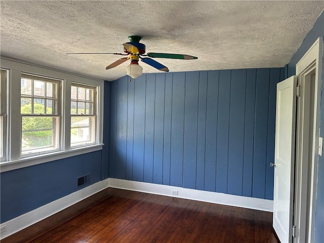 empty room featuring ceiling fan, a textured ceiling, baseboards, visible vents, and dark wood-style floors