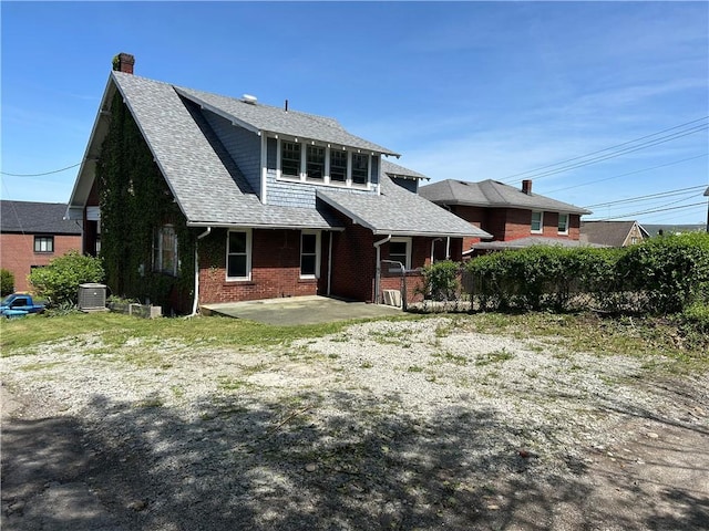 rear view of house featuring a patio, a chimney, brick siding, a shingled roof, and central AC unit