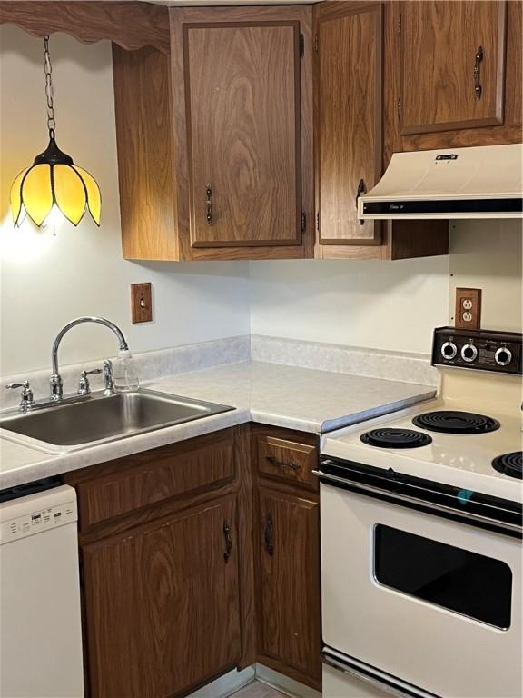 kitchen featuring a sink, white appliances, light countertops, under cabinet range hood, and pendant lighting