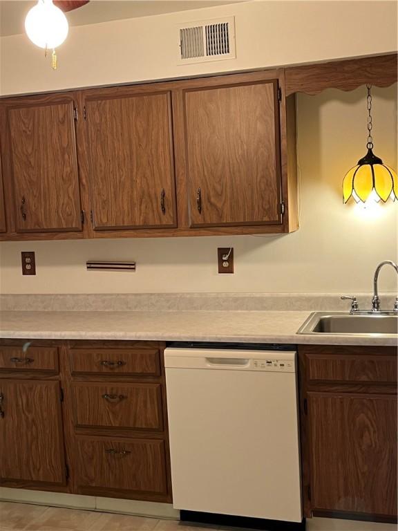kitchen with white dishwasher, light countertops, a sink, and visible vents