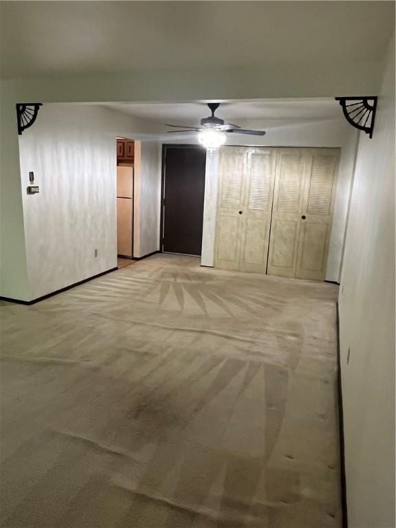unfurnished bedroom featuring freestanding refrigerator, ceiling fan, two closets, and light carpet