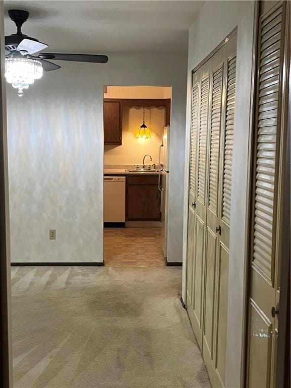 hall featuring baseboards, a sink, and light carpet