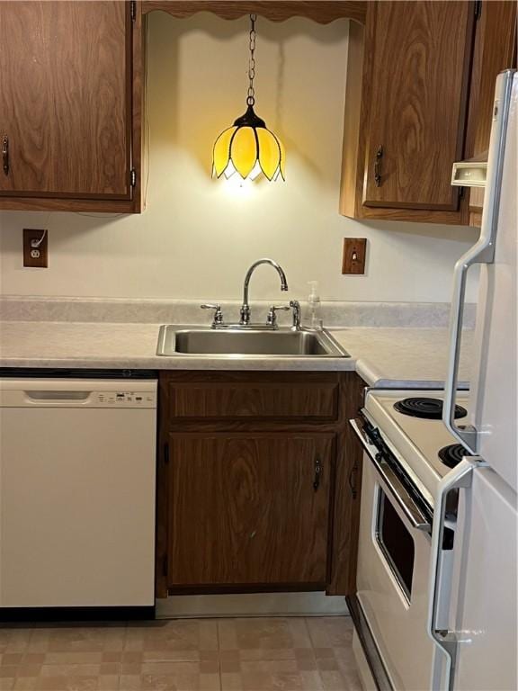 kitchen featuring a sink, light countertops, pendant lighting, and white appliances
