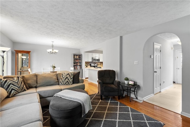 1470 Yorktown Dr, Cecil, PA 15055 - living room featuring a notable chandelier, arched walkways, a textured ceiling, baseboards, and wood finished floors