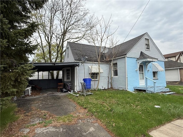 view of side of property featuring a lawn, a shingled roof, an attached carport, and aphalt driveway