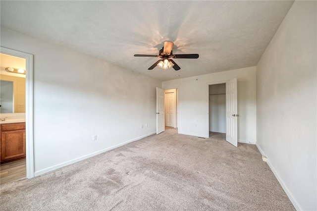 unfurnished bedroom featuring a closet, light carpet, baseboards, connected bathroom, and a ceiling fan