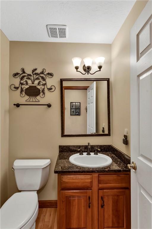 half bath with visible vents, wood finished floors, vanity, baseboards, and toilet