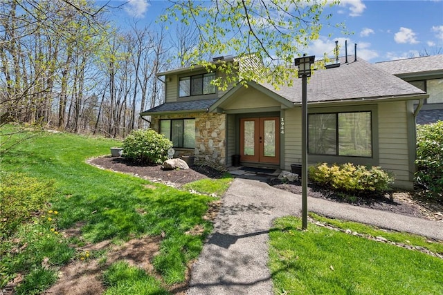 view of front facade with a front lawn, roof with shingles, french doors, and stone siding