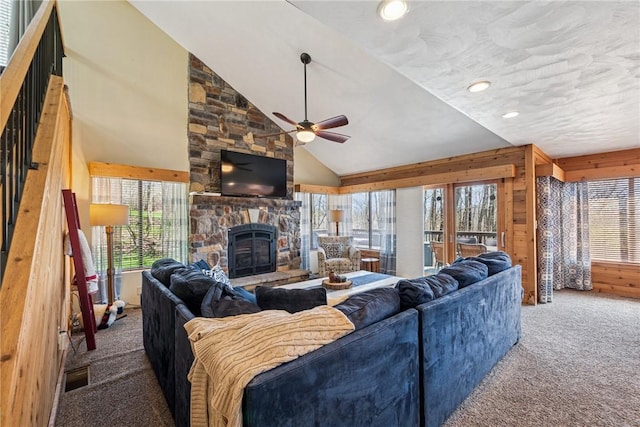 living room featuring carpet flooring, ceiling fan, a stone fireplace, a healthy amount of sunlight, and vaulted ceiling