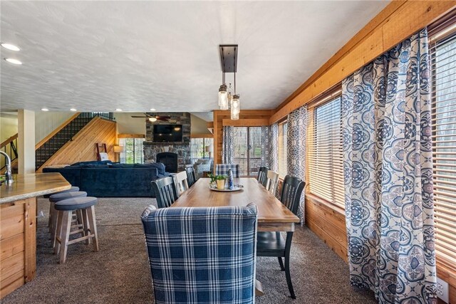 dining room with a stone fireplace, carpet, stairs, and wooden walls