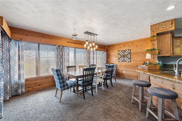 dining space featuring wooden walls, a chandelier, and carpet