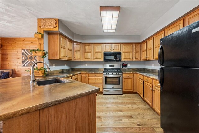 kitchen featuring dark countertops, light wood-type flooring, a sink, black appliances, and a peninsula