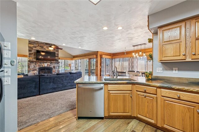 kitchen with a sink, a fireplace, light wood-style flooring, lofted ceiling, and stainless steel dishwasher
