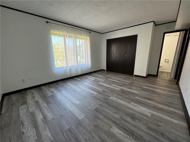 unfurnished bedroom with baseboards, ornamental molding, a textured ceiling, and wood finished floors