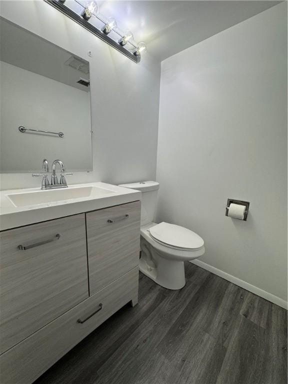 half bath with toilet, baseboards, wood finished floors, and vanity