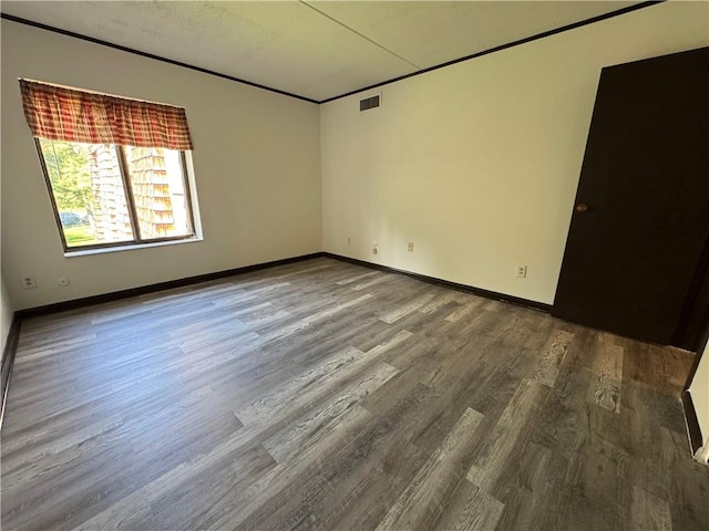 spare room featuring baseboards, ornamental molding, wood finished floors, and visible vents