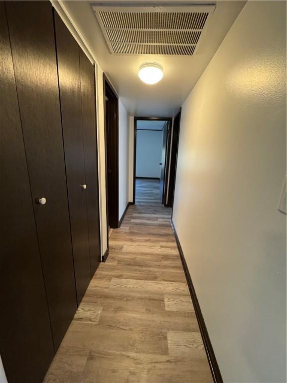 hallway featuring visible vents, light wood finished floors, and baseboards