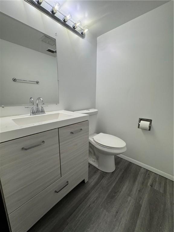 bathroom featuring vanity, toilet, baseboards, wood finished floors, and visible vents