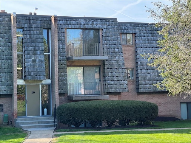 view of front of property featuring brick siding, mansard roof, and a balcony