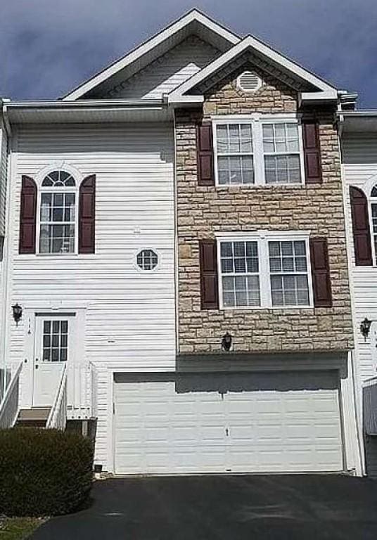 view of front of home with an attached garage, driveway, and stone siding