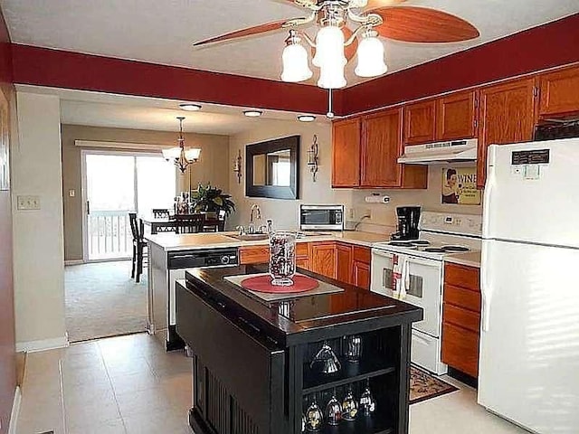 kitchen featuring ceiling fan with notable chandelier, brown cabinetry, under cabinet range hood, and white appliances