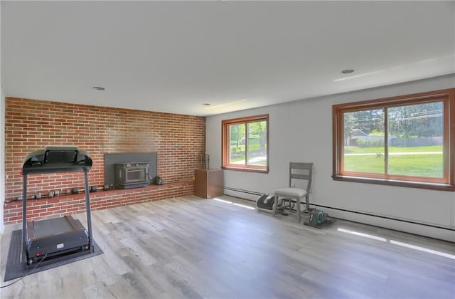 exercise room with a wood stove, wood finished floors, and baseboard heating