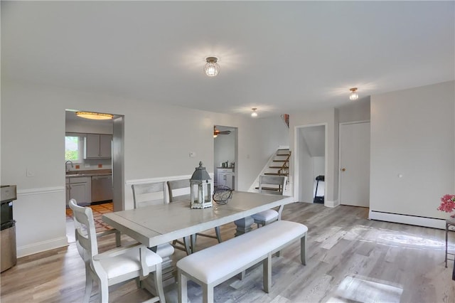 dining room featuring light wood-type flooring, baseboard heating, and stairway
