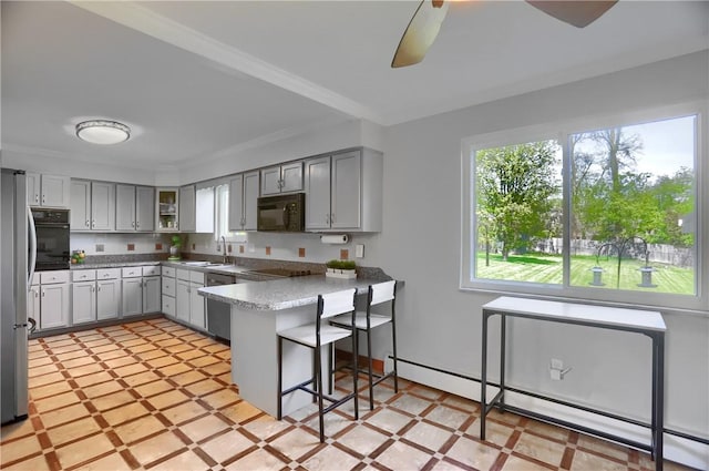 kitchen with a peninsula, a breakfast bar area, a baseboard radiator, a sink, and black appliances