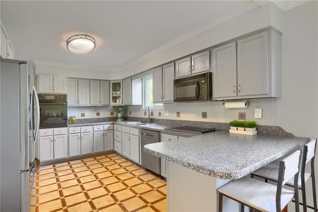 kitchen featuring crown molding, a sink, black appliances, a peninsula, and a breakfast bar