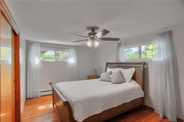 bedroom with multiple windows, baseboard heating, and light wood-style flooring