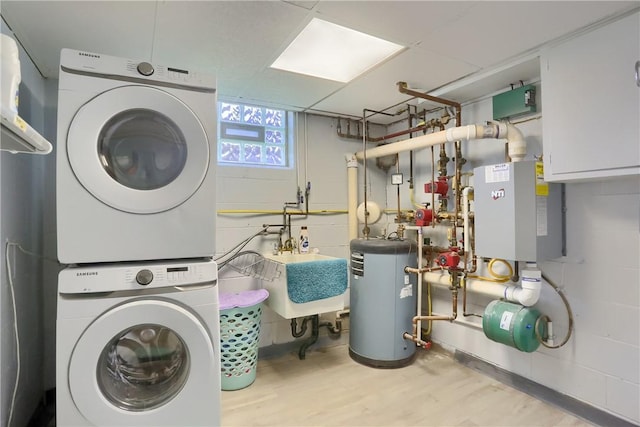 clothes washing area with laundry area, wood finished floors, stacked washer / dryer, a sink, and water heater